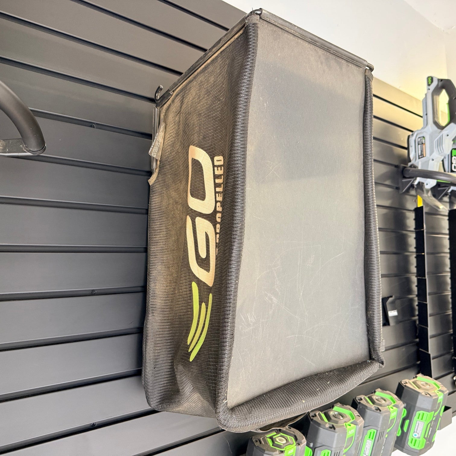 PartForge mounting bracket holding a black EGO mower bag on a Gladiator GearWall panel in a garage.